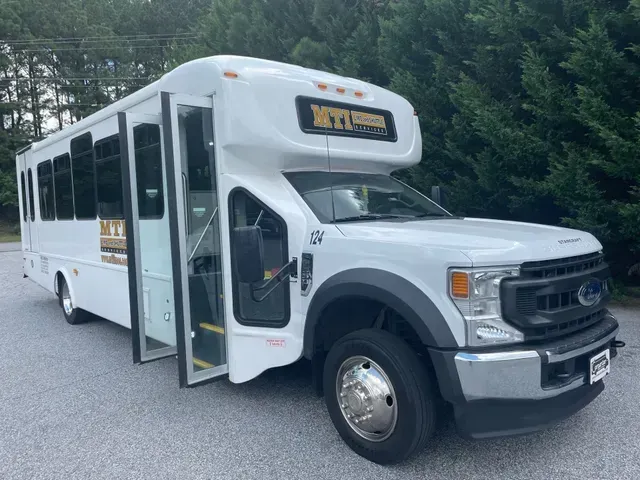 White school bus with open door parked outdoors near trees