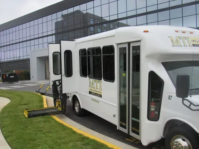 White shuttle van with wheelchair lift parked outside a glass office building