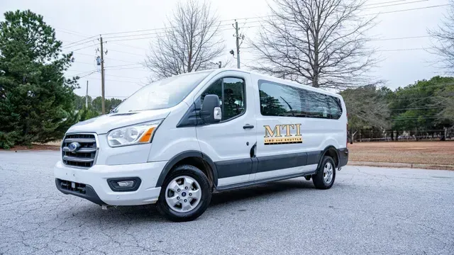 Silver passenger van parked on a gravel lot with trees in the background