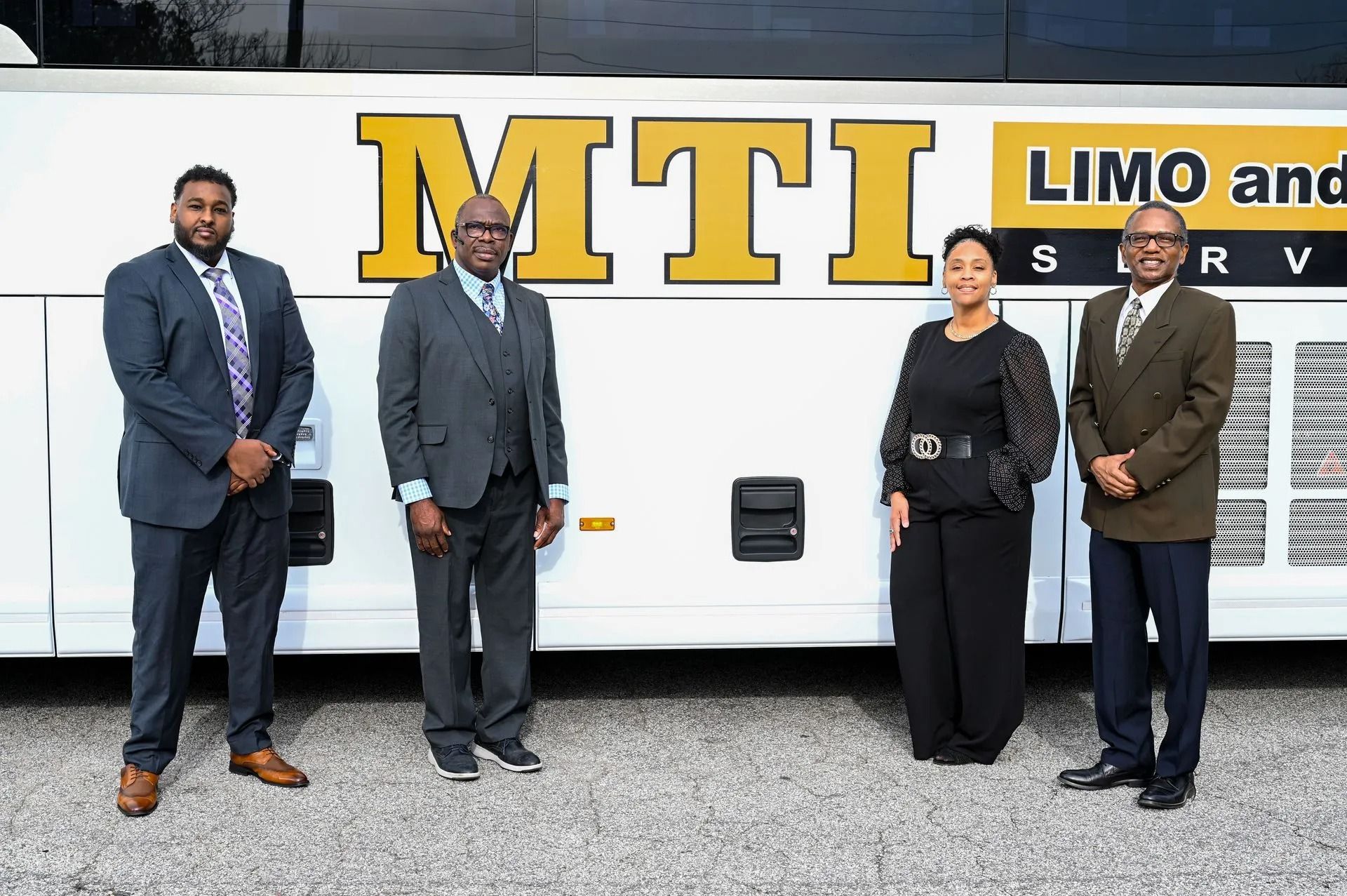 Four people in business attire stand in a line in front of a white bus with 