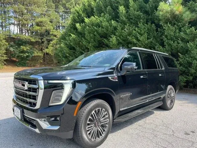 Black GMC SUV parked on a paved lot beside green trees in daylight