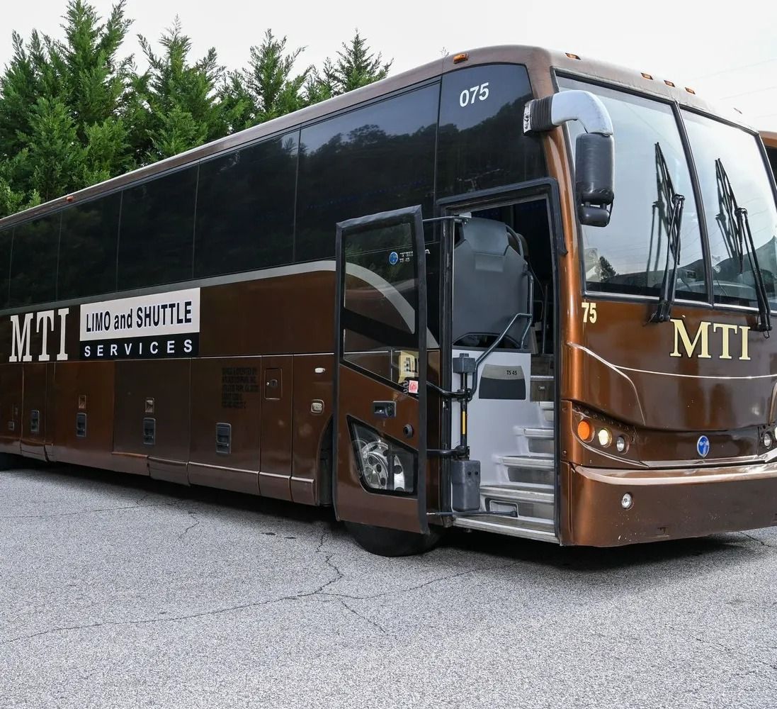 A brown MTI coach bus parked on a gravel lot with its passenger door open, viewed from the front three-quarter angle.