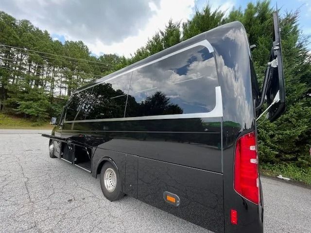 A shiny black bus parked outdoors, with its side luggage compartment open and a rear door slightly ajar.
