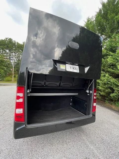 The rear of a black Sprinter-style van with its large, upward-opening cargo door raised, revealing an empty storage area.