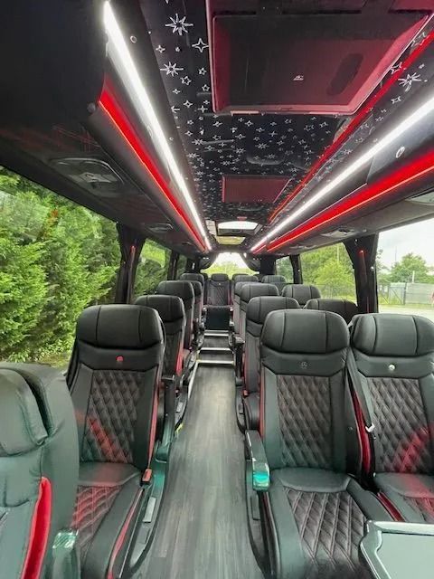 Interior of a bus with rows of black, diamond-stitched leather seats, red LED strip lighting, and a star-pattern ceiling.