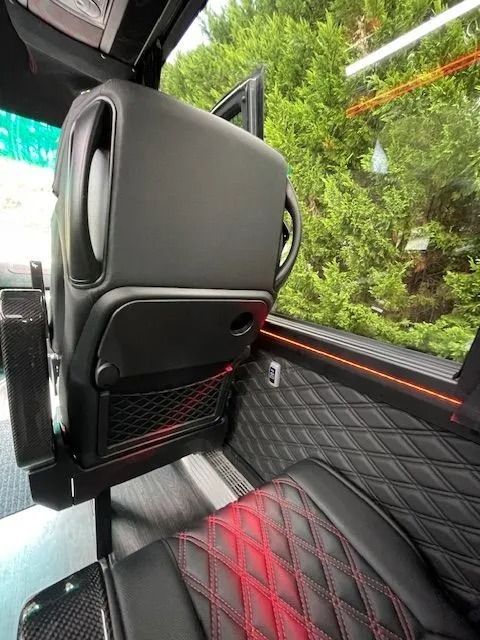 Interior of a luxury bus featuring black leather seats with red diamond-stitch accents and a dark, modern cabin design.