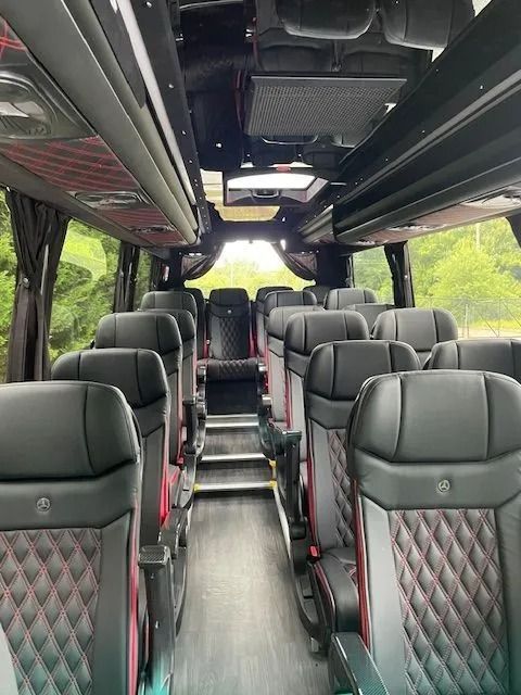 Interior view of a bus with rows of black leather seats featuring red diamond-pattern stitching and wood-look flooring.