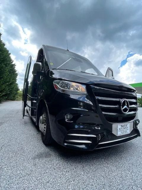 A black Mercedes-Benz Sprinter van parked outdoors with its driver-side door open under a cloudy sky.