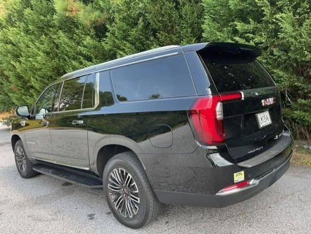 A black GMC Yukon XL SUV parked on an asphalt surface with trees in the background.