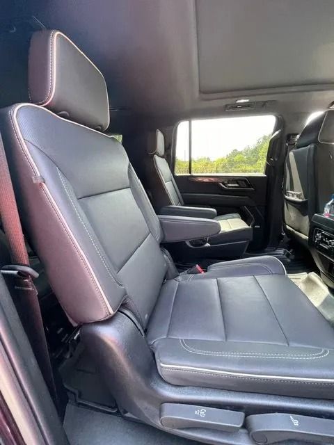 The interior of a vehicle featuring dark leather captain's chairs with light-colored stitching and armrests.