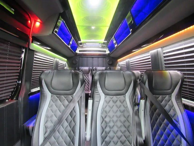 Luxury van interior featuring three rows of black and grey diamond-stitched leather seats under vibrant LED ceiling lights.