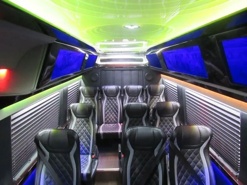 Luxury shuttle bus interior featuring diamond-stitched leather seating, blue overhead screens, and vibrant green lighting.