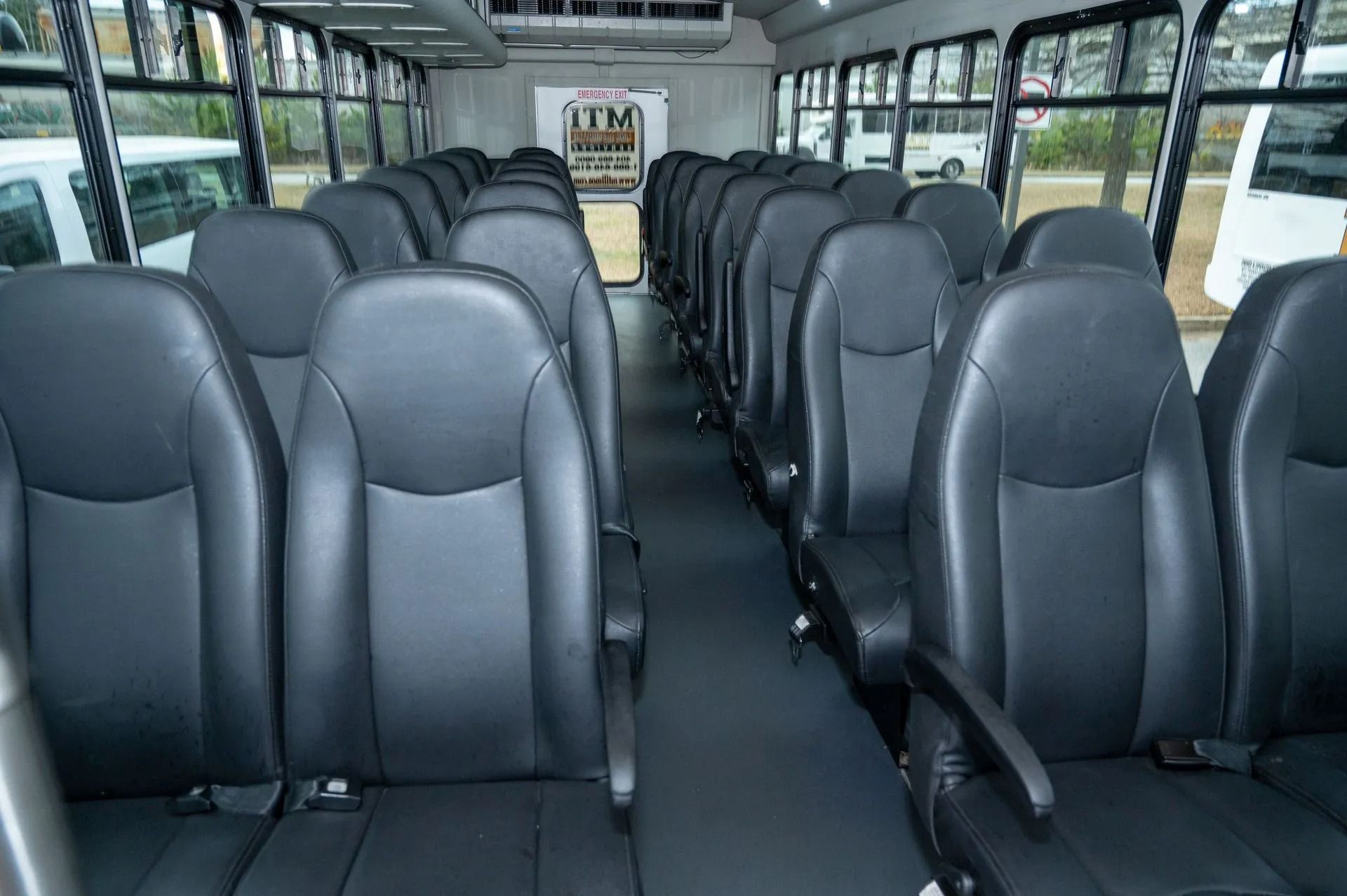 The interior of a shuttle bus featuring rows of empty black leather seats facing forward on either side of an aisle.