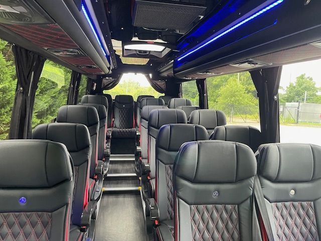 The interior of a bus with rows of black leather seats featuring diamond-patterned stitching and blue accent lighting.