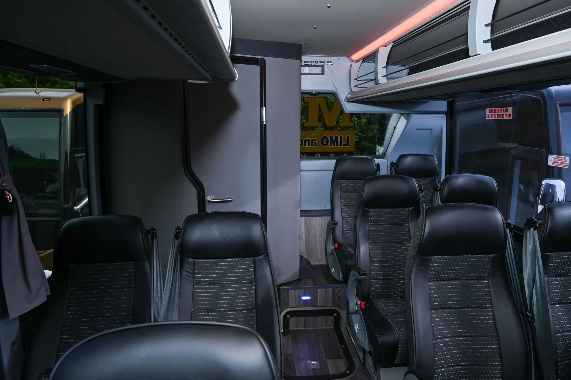 Interior of a bus featuring rows of dark leather seats and overhead storage racks, looking toward the rear exit.