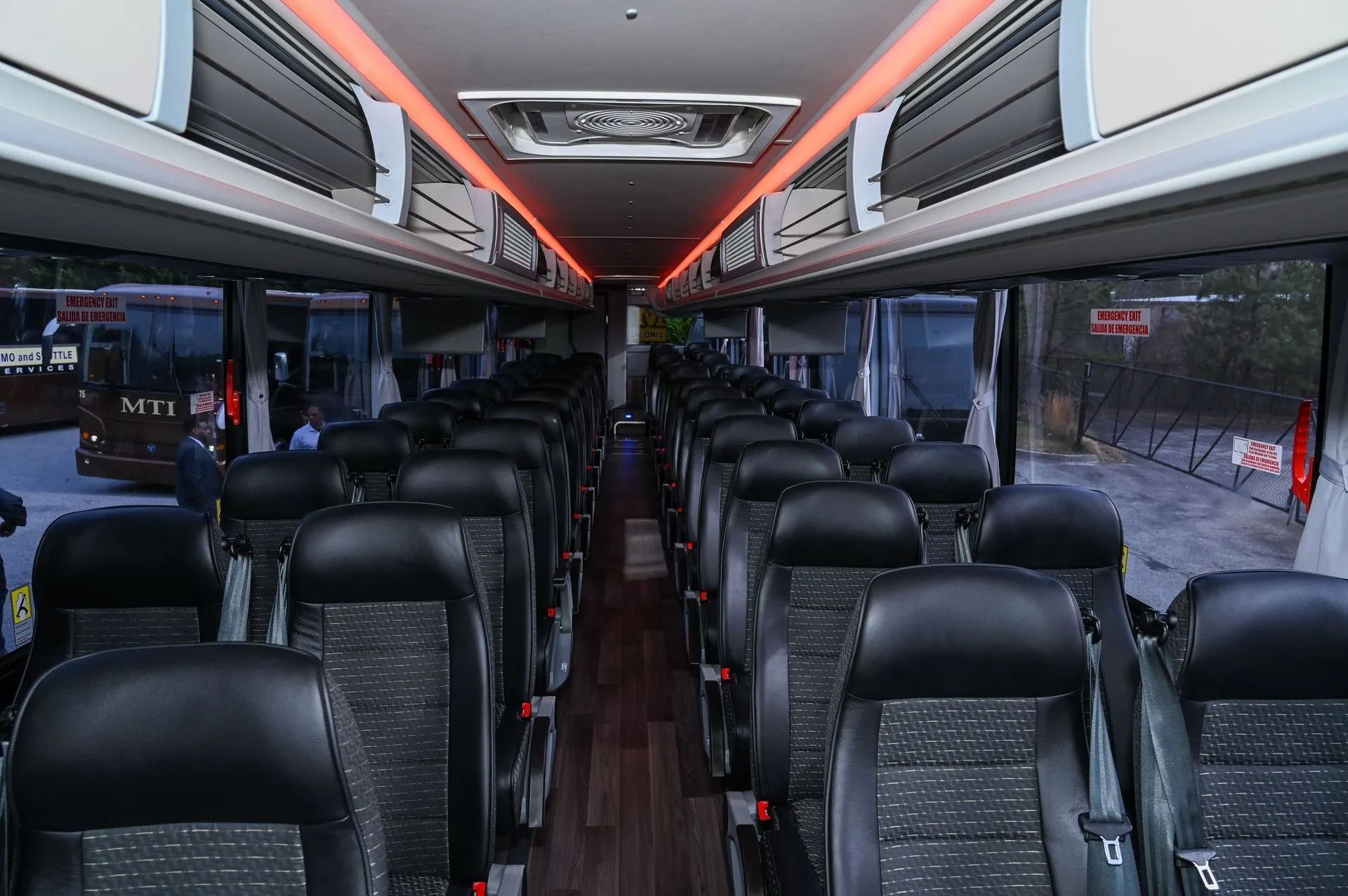 The interior of a bus with rows of black seats on either side of a center aisle and warm accent lighting on the ceiling.