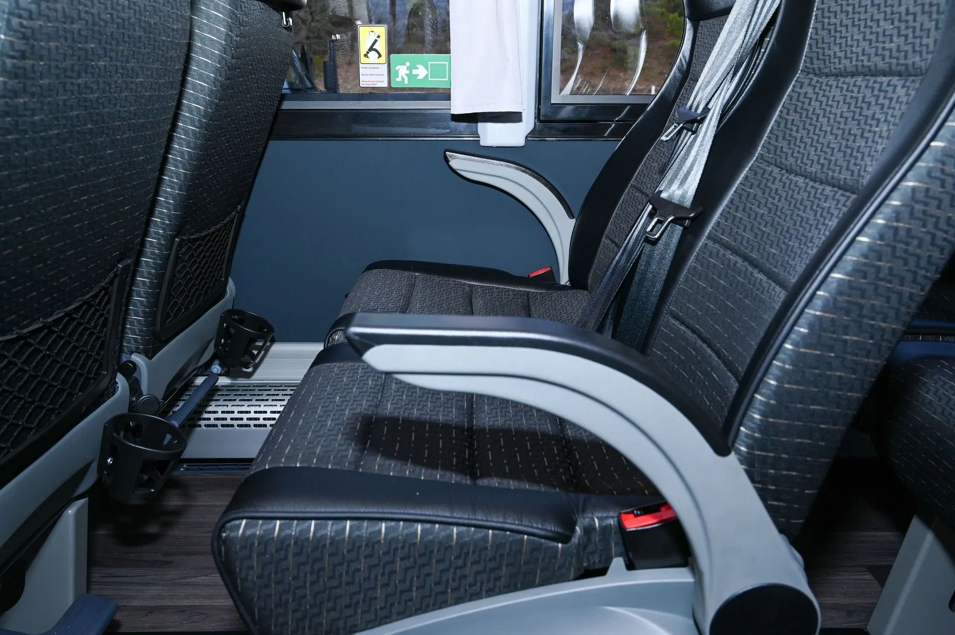 Interior of a bus featuring dark grey patterned seats, black seatbelts, and a cup holder on the aisle side.