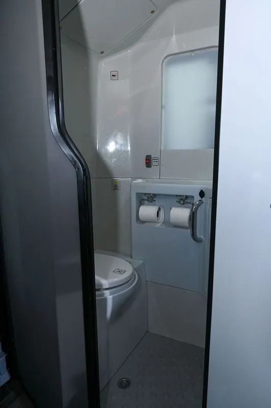 A view inside a narrow, sterile white airplane restroom featuring a toilet, two toilet paper rolls, and a small mirror.
