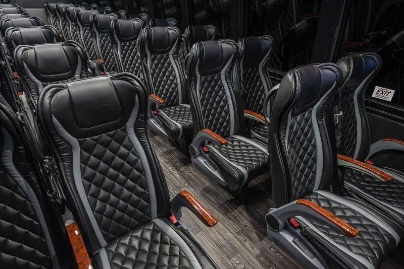 Rows of black quilted leather bus seats with orange armrests in a luxury vehicle interior