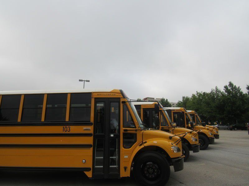 A row of yellow school buses parked in a lot under a cloudy sky.