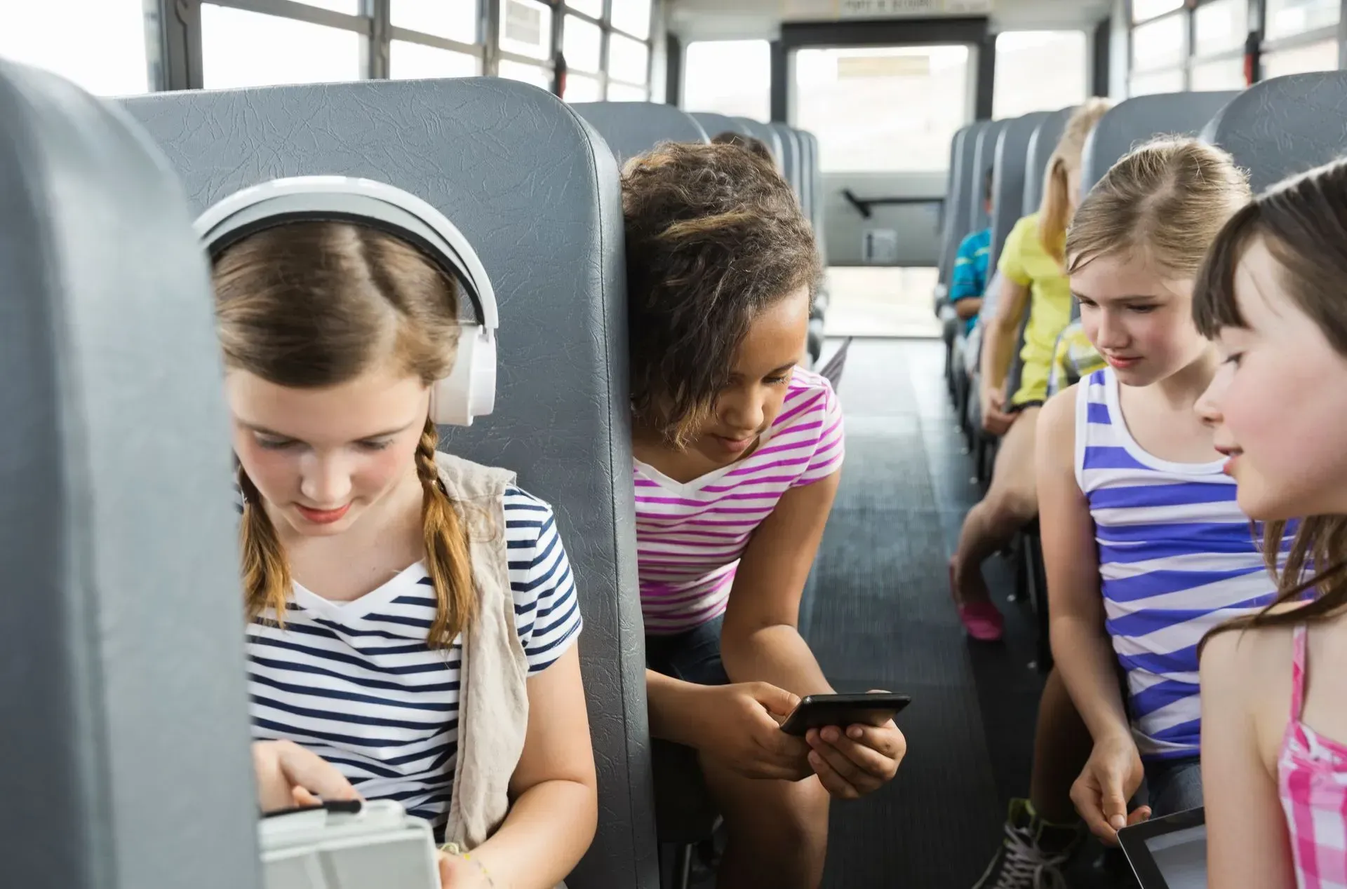 Children seated on a bus, looking at a tablet together during a ride