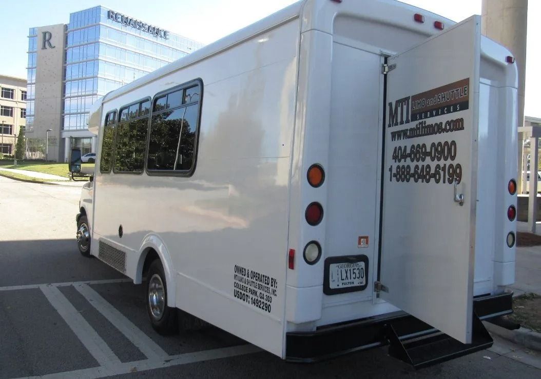 A white box truck parked on a street in front of a modern glass office building with its rear cargo door open.