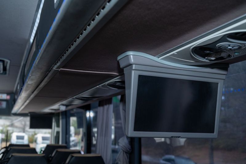 Bus interior with overhead folding monitor screens and dark seats.