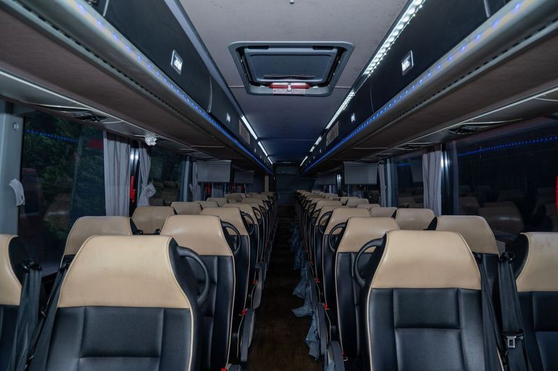 Empty coach bus interior with rows of tan and black seats and overhead lighting.