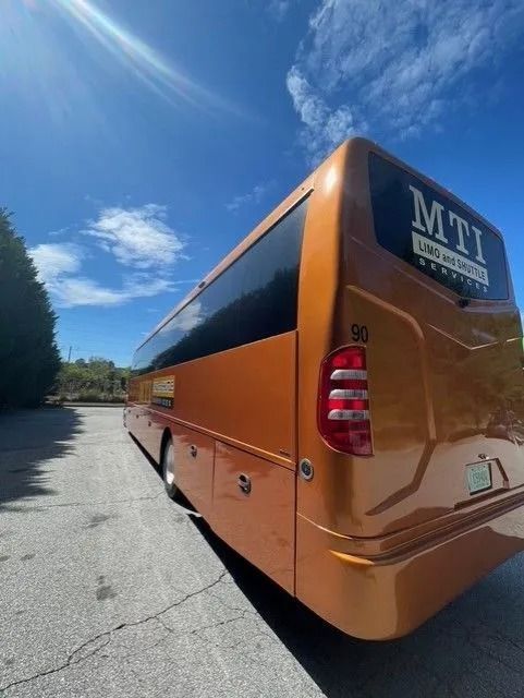 A metallic orange motorcoach bus parked on a paved lot under a clear blue sky.
