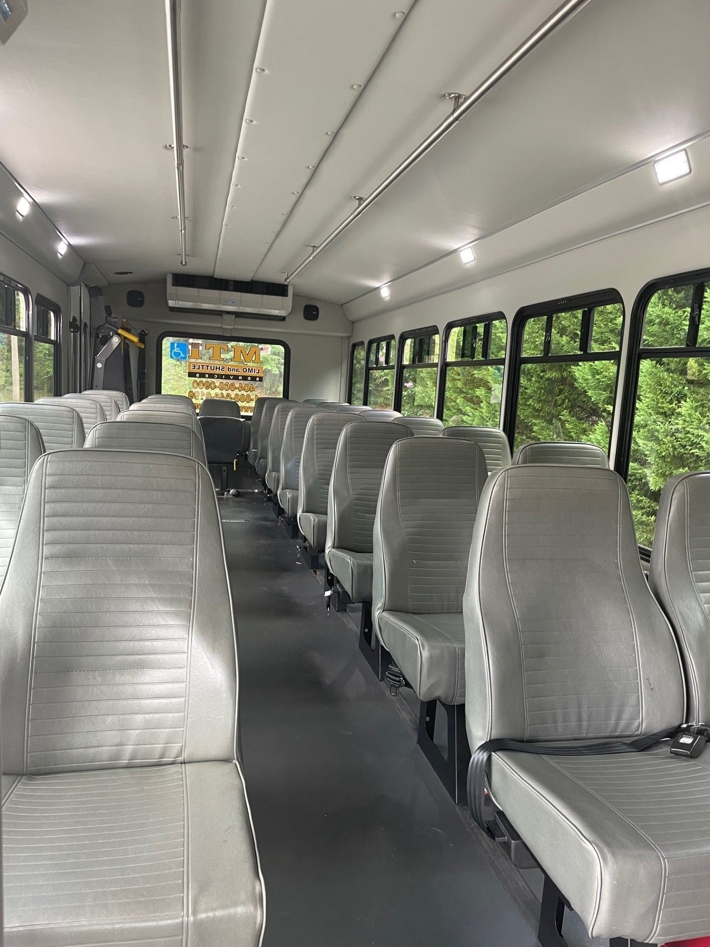 Interior view of a bus with rows of grey passenger seats facing forward and overhead lighting lining the ceiling.