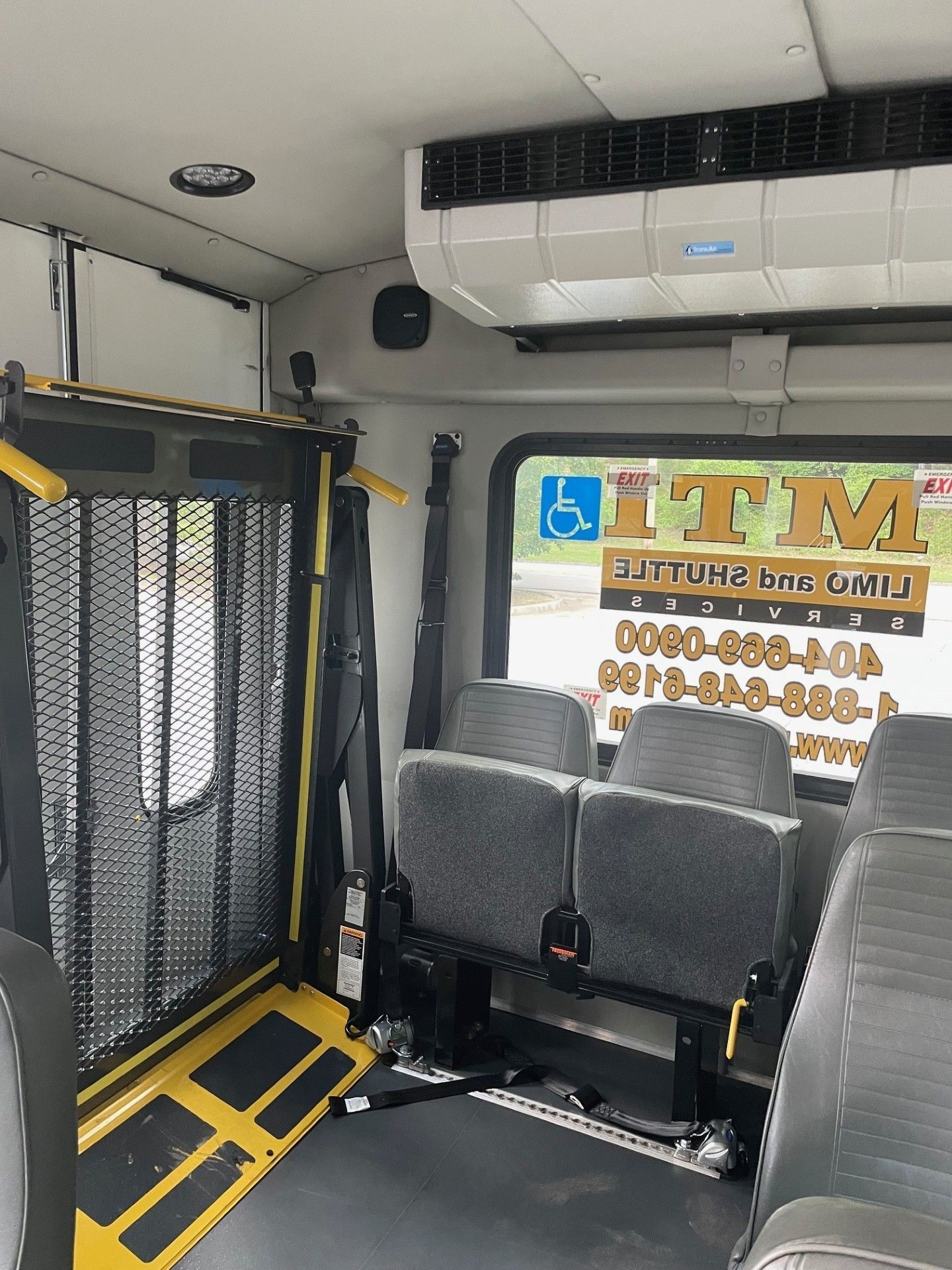 Interior of a shuttle bus featuring a wheelchair lift platform, gray seating, and an MTI logo on the rear window.