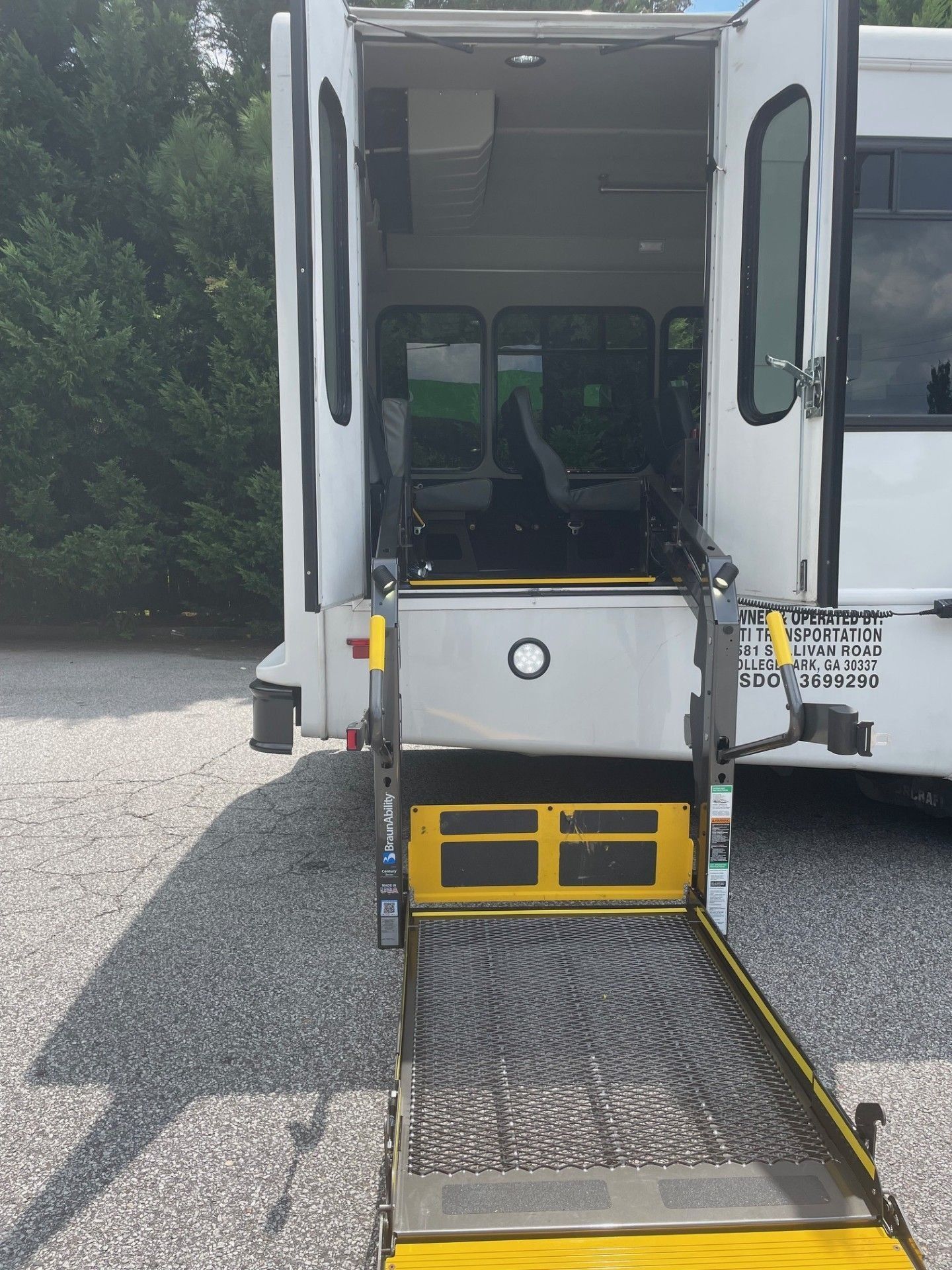 A white shuttle bus with an extended yellow wheelchair lift deployed at the rear open double doors.