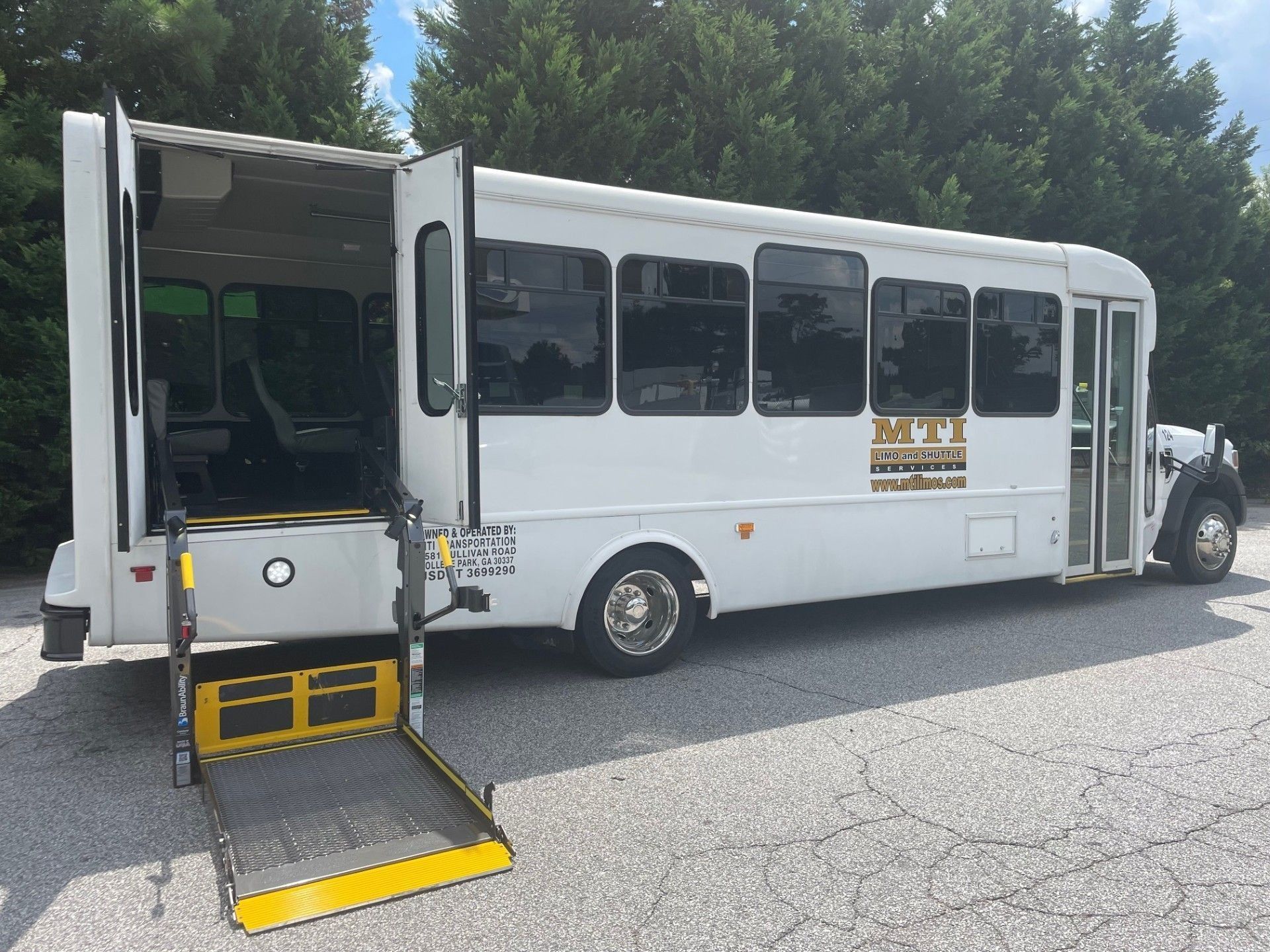 A white bus parked outdoors with its side doors open and a wheelchair lift lowered to the ground.