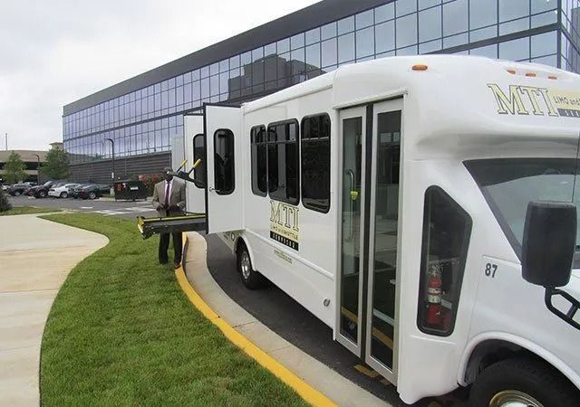 A white shuttle bus with an extended wheelchair lift parked near a modern office building.