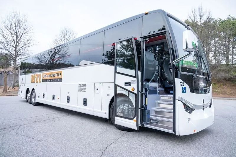 White MTT motorcoach parked outdoors with its front entrance door open, revealing interior steps.