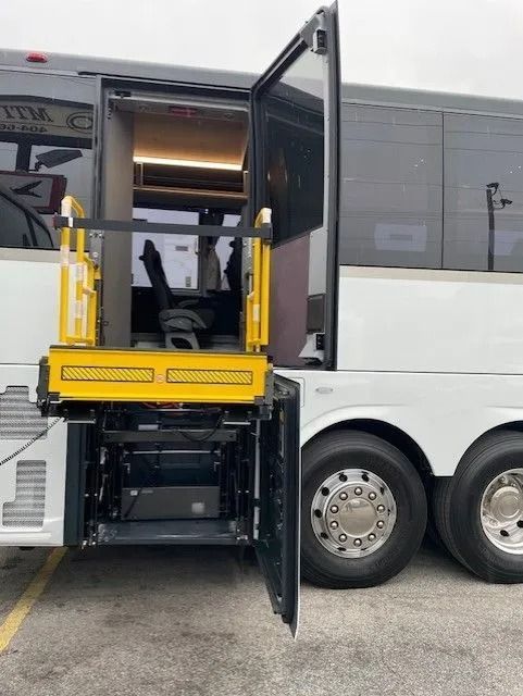 A yellow wheelchair lift deployed from the side door of a white bus parked on a paved lot.
