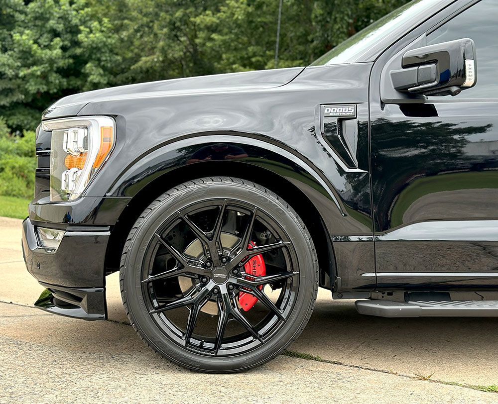 Black Ford F-150 truck with black rims, red brake calipers, and a black exterior, parked outdoors.