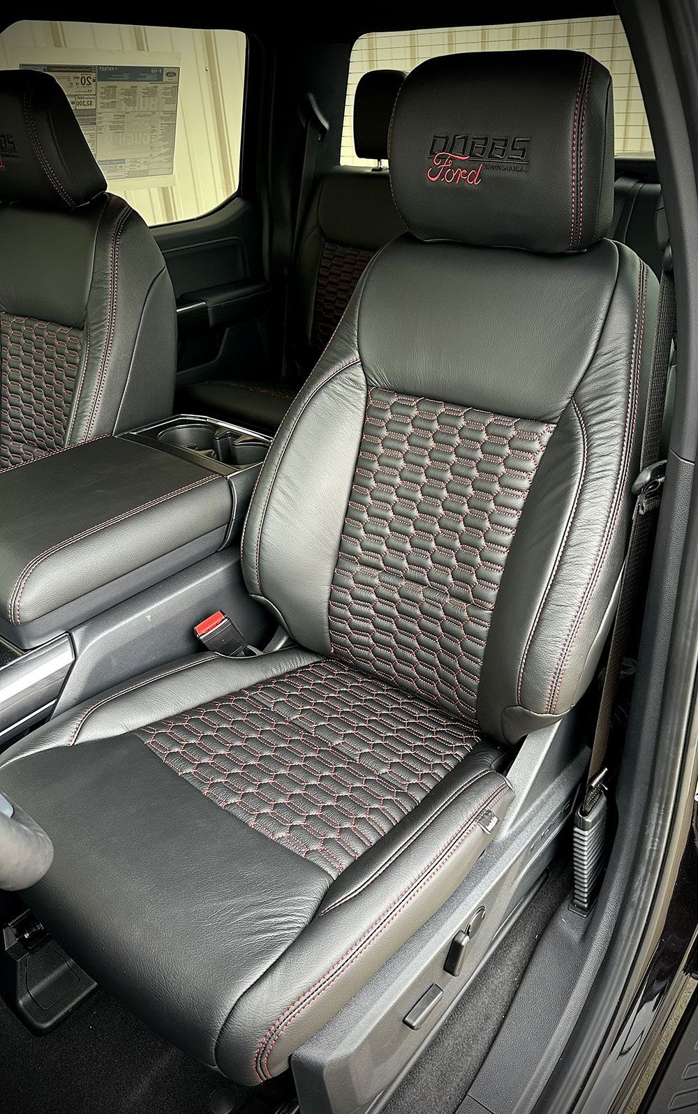 Black and gray leather truck seat with red stitching and headrest logo.