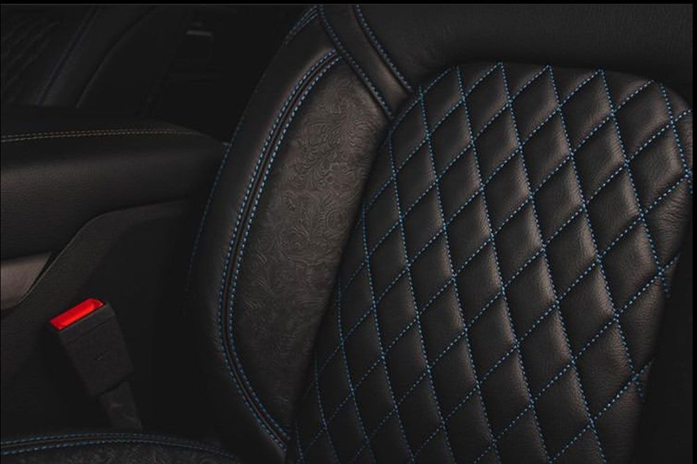 Black car seat with diamond-stitched pattern and blue thread. Red seatbelt buckle visible.