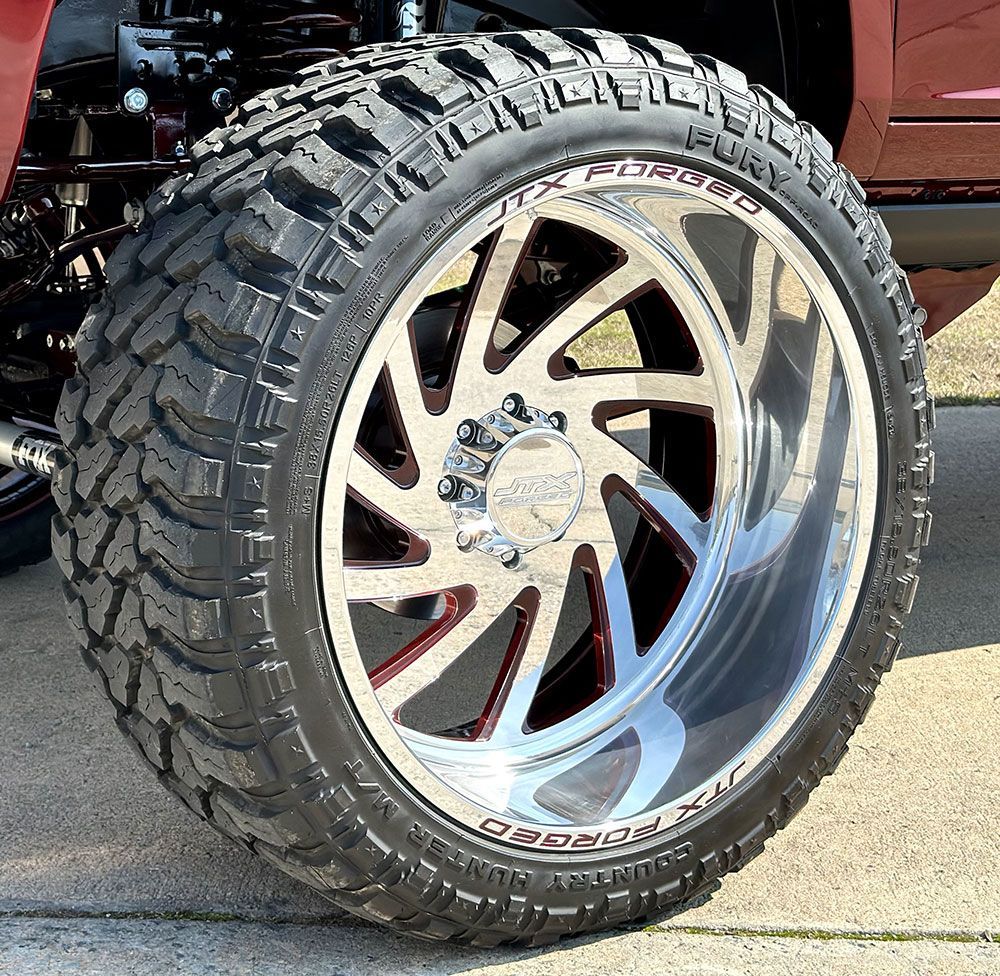 Close-up of a large truck tire and chrome rim. Black tire tread, polished silver and red rim, and shiny center cap.