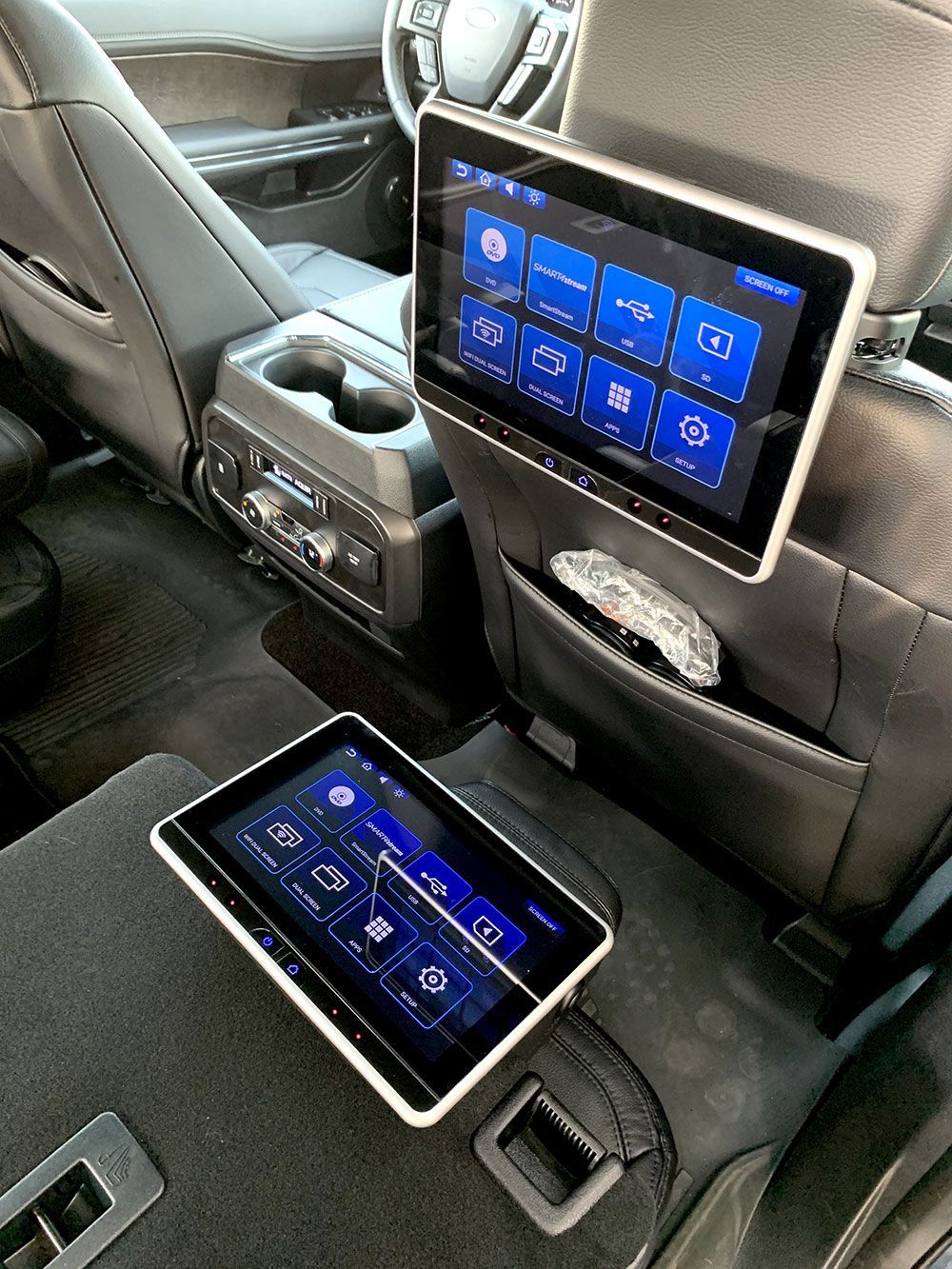 Rear vehicle interior with two touch-screen displays, cup holders, and control panel.