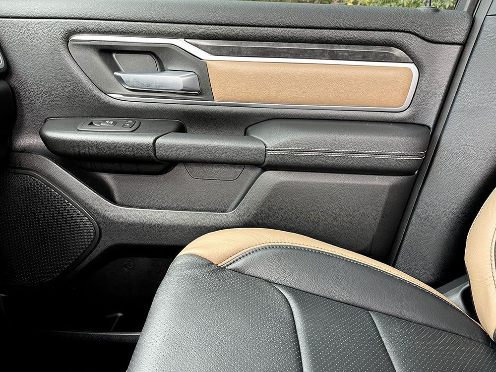 Car door interior, black and tan, with handle, controls, and part of a seat.