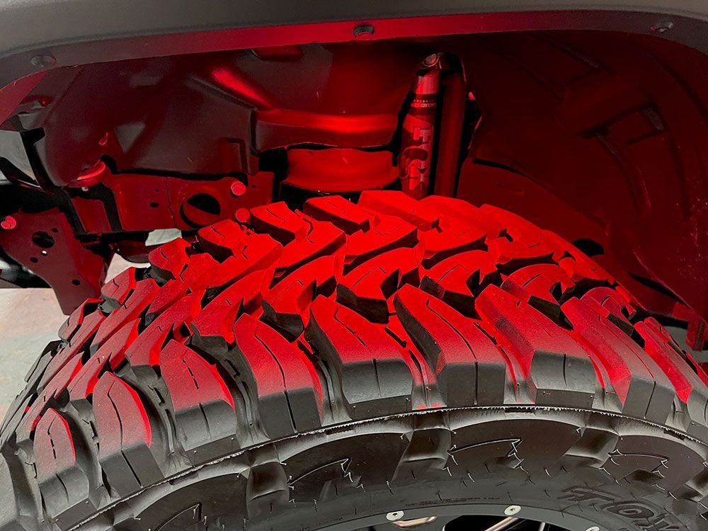 Red underglow illuminating a large off-road tire and vehicle undercarriage.
