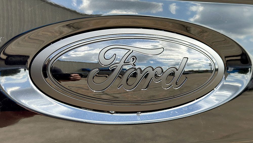 Chrome Ford emblem on a vehicle, reflecting the sky.