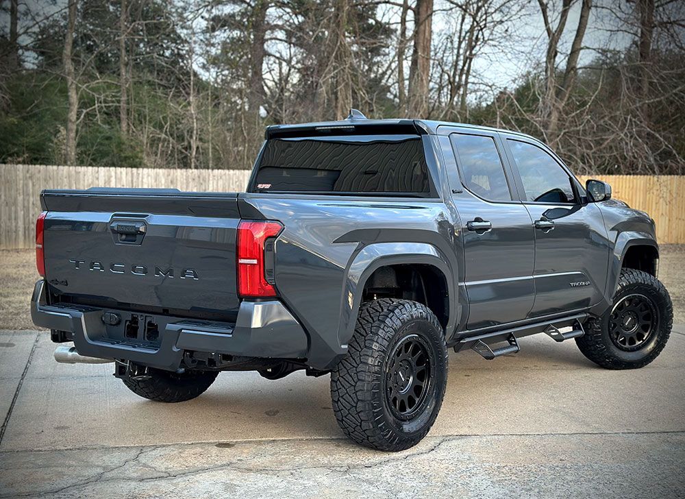 Gray Toyota pickup truck parked outdoors, with large tires, a black bed cover, and tinted windows.