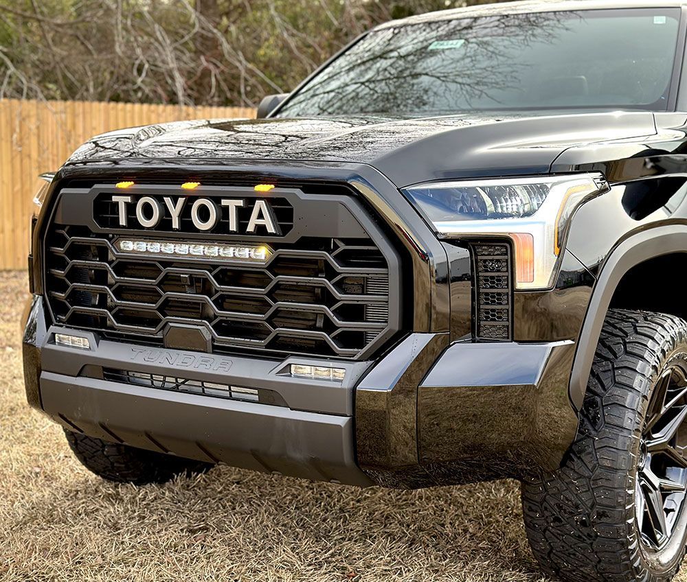 Black Toyota Tundra truck with custom grille and LED lights in front of a fence.