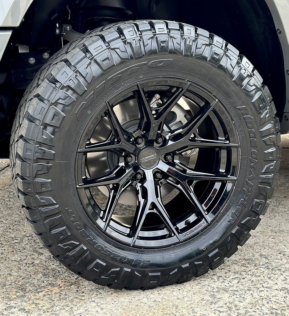 Black tire with black rim on a vehicle, outdoors.