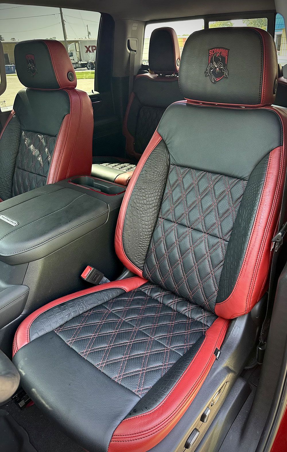 Black and red leather car seats with diamond stitching and headrest logo, centered in the car.