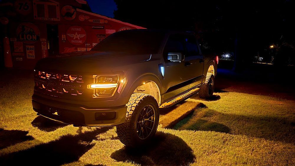 Dark pickup truck with glowing amber lights parked outside at night.