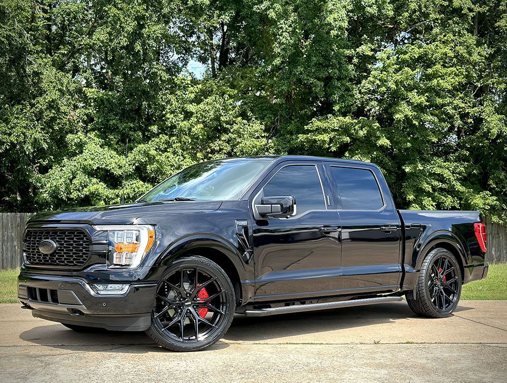 Black Ford F-150 pickup truck with tinted windows, black rims, and red brake calipers parked outside.